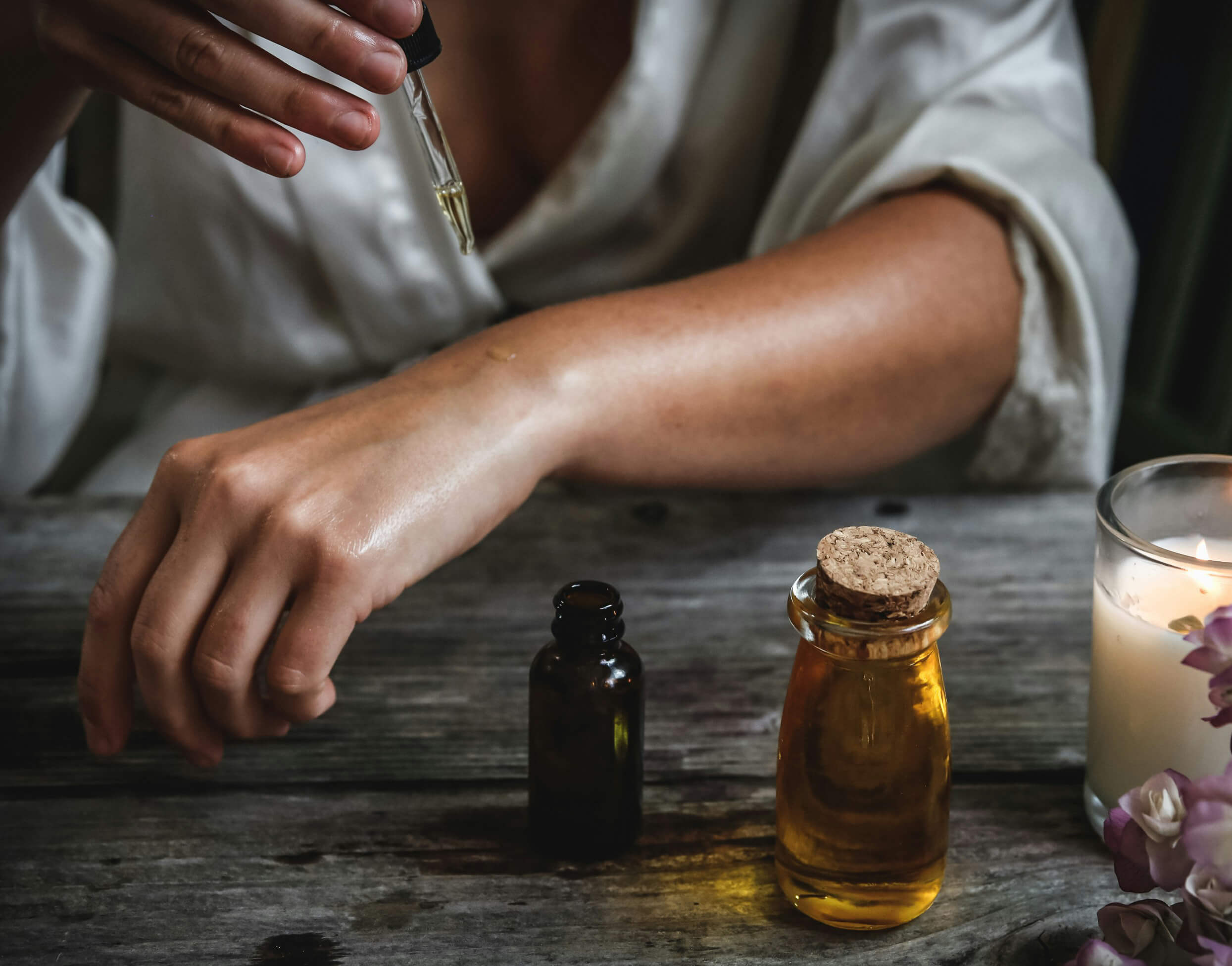 Persoon die essentiële olie of serum aanbrengt op de huid naast een brandende kaars